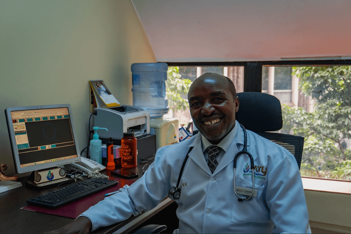 a man in a white coat and tie sitting at a desk with a computer